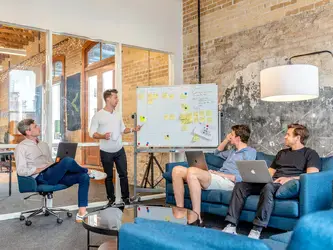 three men sitting while using laptops and watching a man beside a whiteboard
